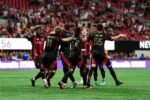 Jugadores del Atlanta United celebran con Giuliano Galoppo tras un gol en el Mercedes-Benz Stadium, con las gradas llenas al fondo.
