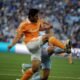 Brian Ching, con la camiseta naranja del Houston Dynamo, lanza una patada con la pierna derecha para controlar el balón ante la marca de un rival.