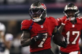 Bucky Irving, corredor de los Buccaneers de Tampa Bay, avanza con el balón durante una carrera en el AT&T Stadium, con un compañero detrás.