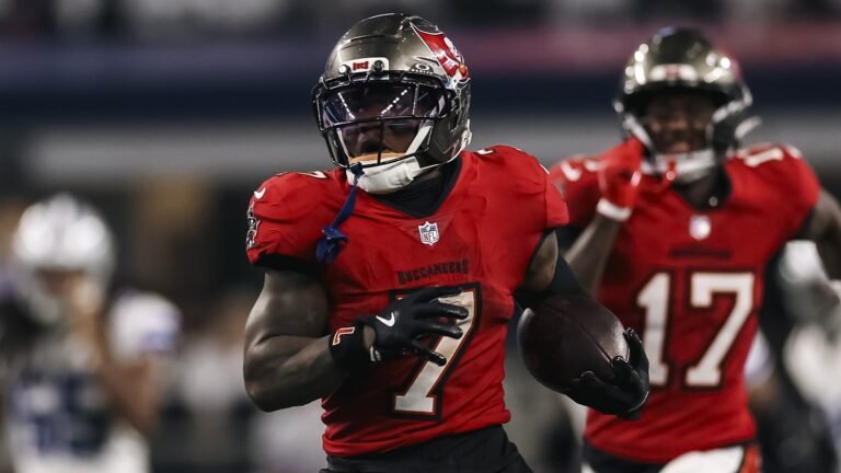 Bucky Irving, corredor de los Buccaneers de Tampa Bay, avanza con el balón durante una carrera en el AT&T Stadium, con un compañero detrás.