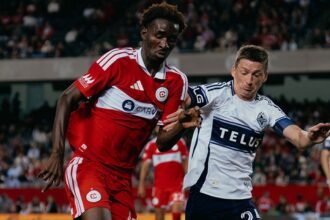 Un jugador del Chicago Fire de camiseta roja disputa el balón con un jugador de Vancouver Whitecaps en un partido de la MLS.