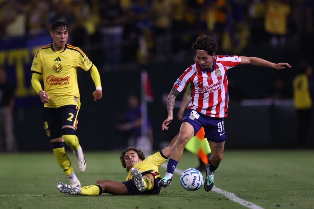 Un futbolista de Chivas conduce el balón mientras un rival del América cae al césped durante el Clásico Nacional amistoso en Oakland.