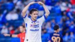 Un futbolista de Cruz Azul con los brazos sobre la cabeza durante un partido, con el uniforme blanco del club.