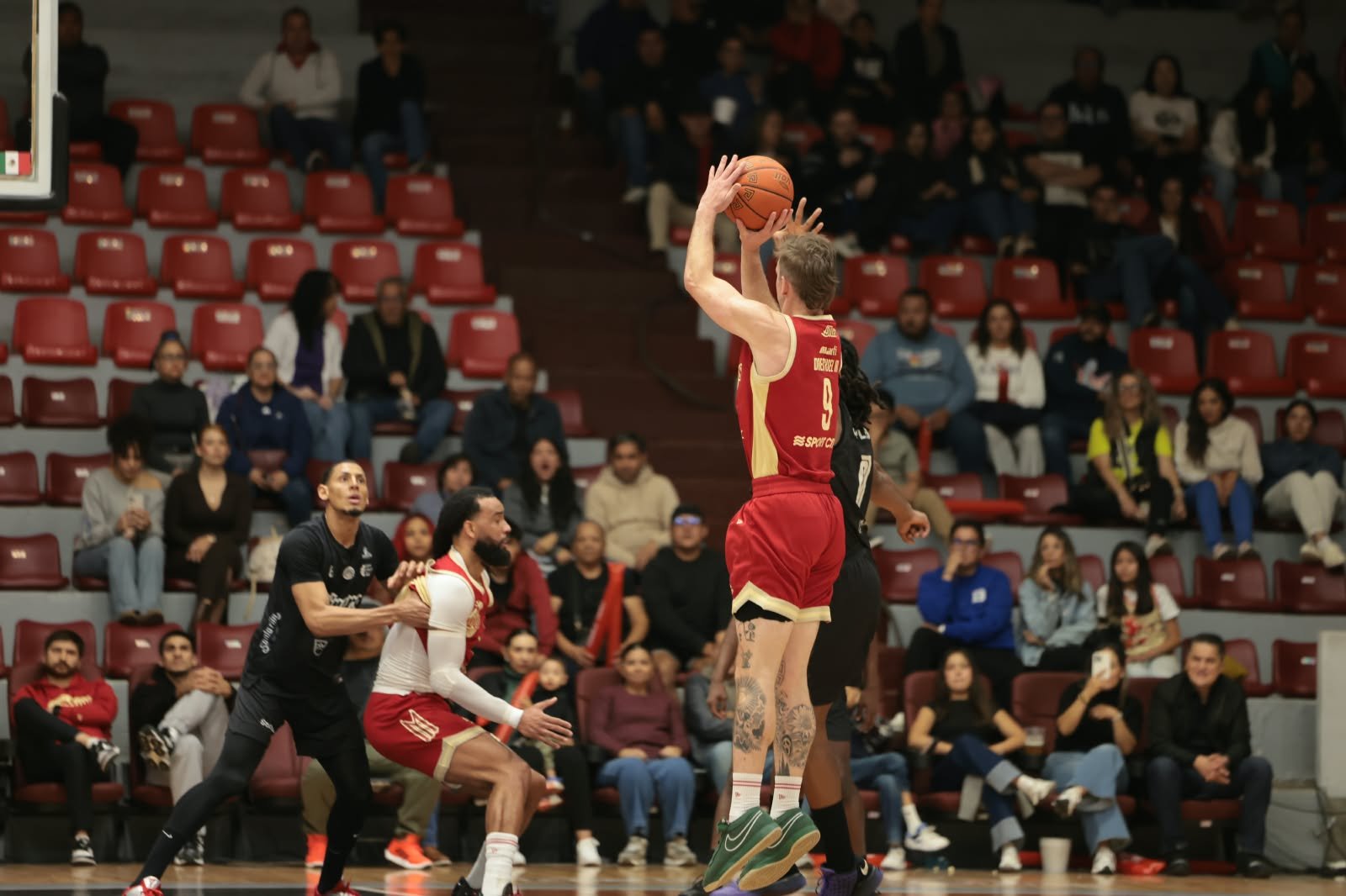 Un jugador de Diablos Rojos con el número 9 lanza un triple en el Gimnasio Marcelino González durante el Juego 1 del Play-In.
