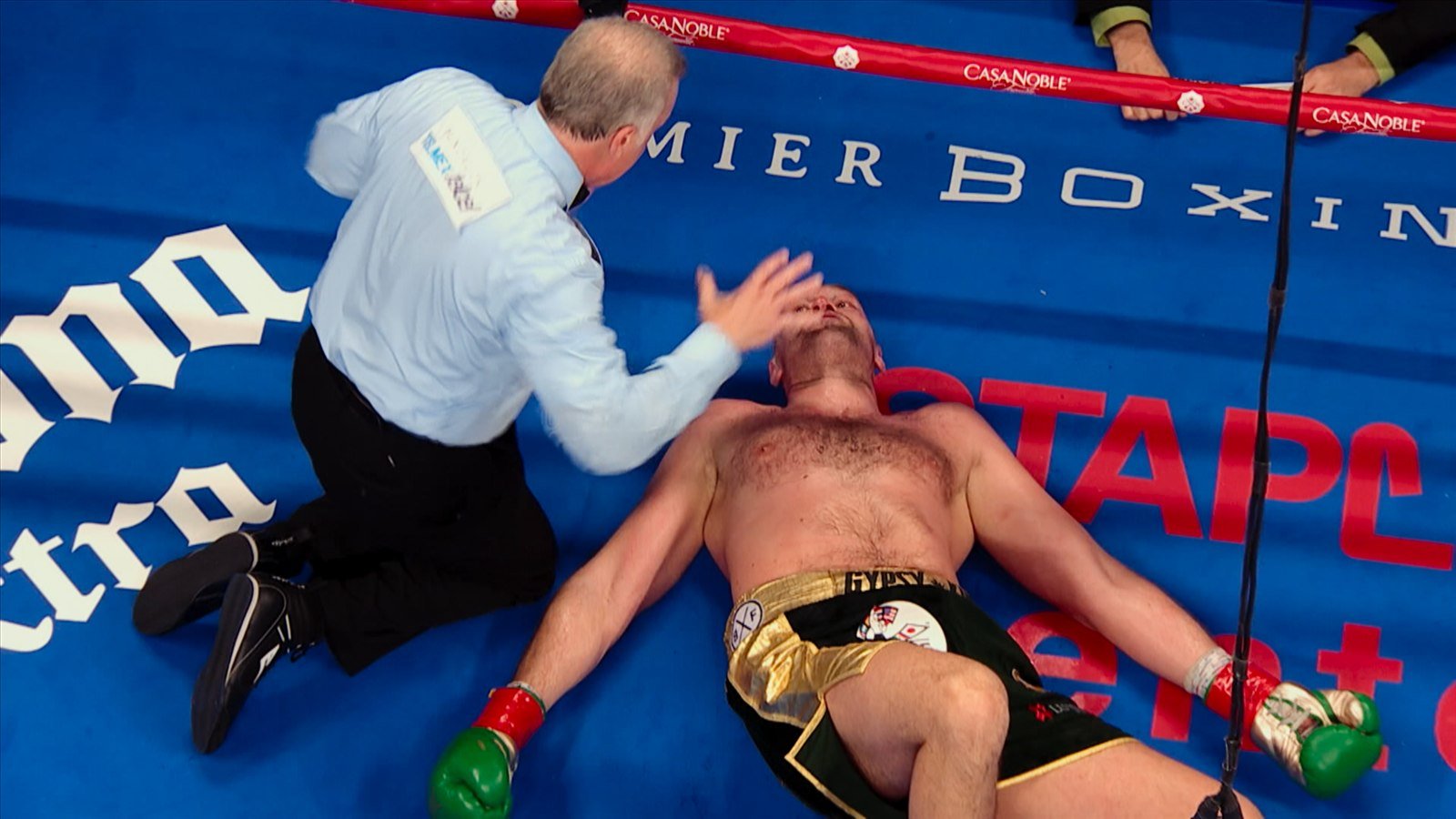 Escena del tráiler del documental TYSON FURY, de Netflix, con un boxeador en la lona atendido por el réferi
