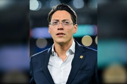 Enrique Nieto Junco, directivo de la Federación Mexicana de Futbol, con lentes y traje azul con el escudo de la FMF en la solapa, en un estadio.