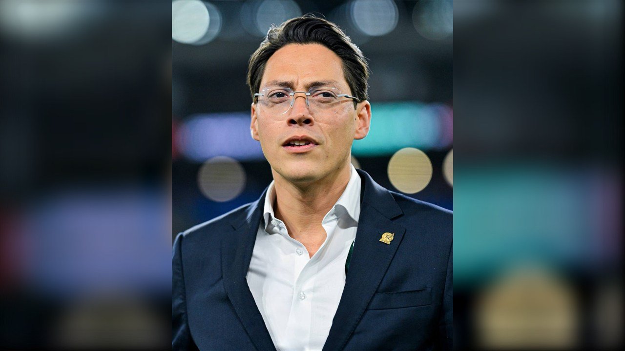 Enrique Nieto Junco, directivo de la Federación Mexicana de Futbol, con lentes y traje azul con el escudo de la FMF en la solapa, en un estadio.