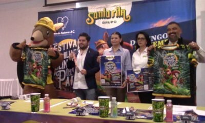 Presentación del Festival Familiar Colinas del Padre 2026 con la botarga del armadillo, playeras del evento y carteles, frente a la manta de Grupo Santa Rita