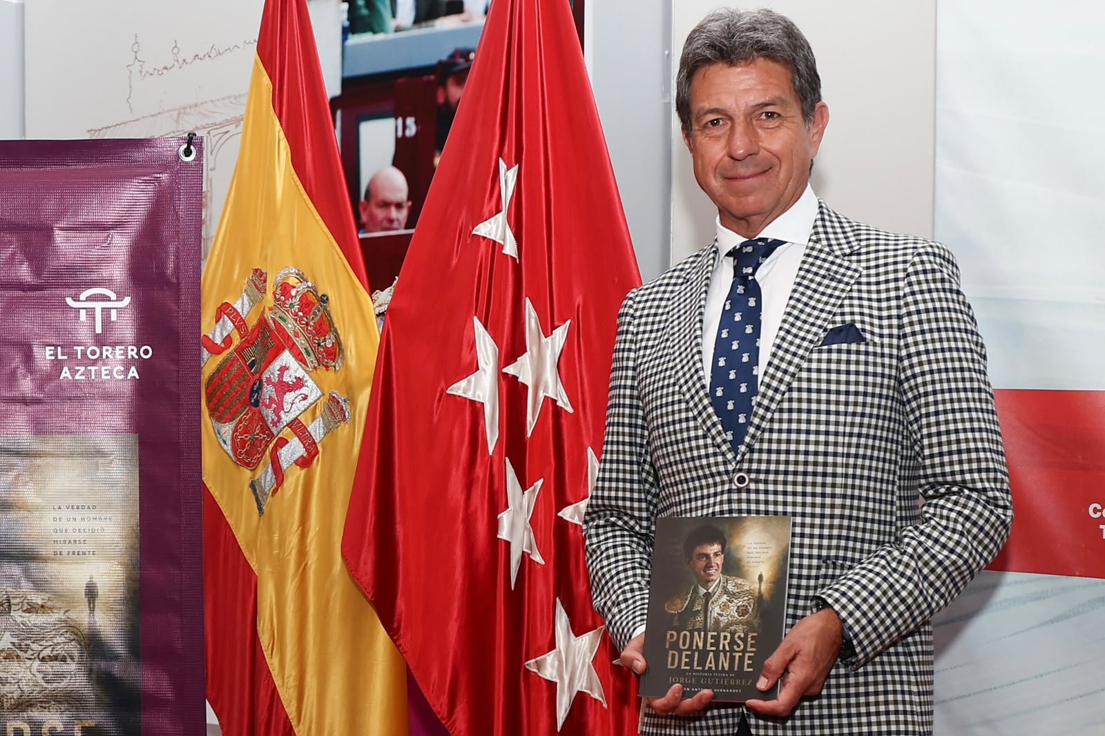Juan Antonio Hernández, «El Torero Azteca», posa con un ejemplar de «Ponerse Delante» frente a las banderas de España y de la Comunidad de Madrid.