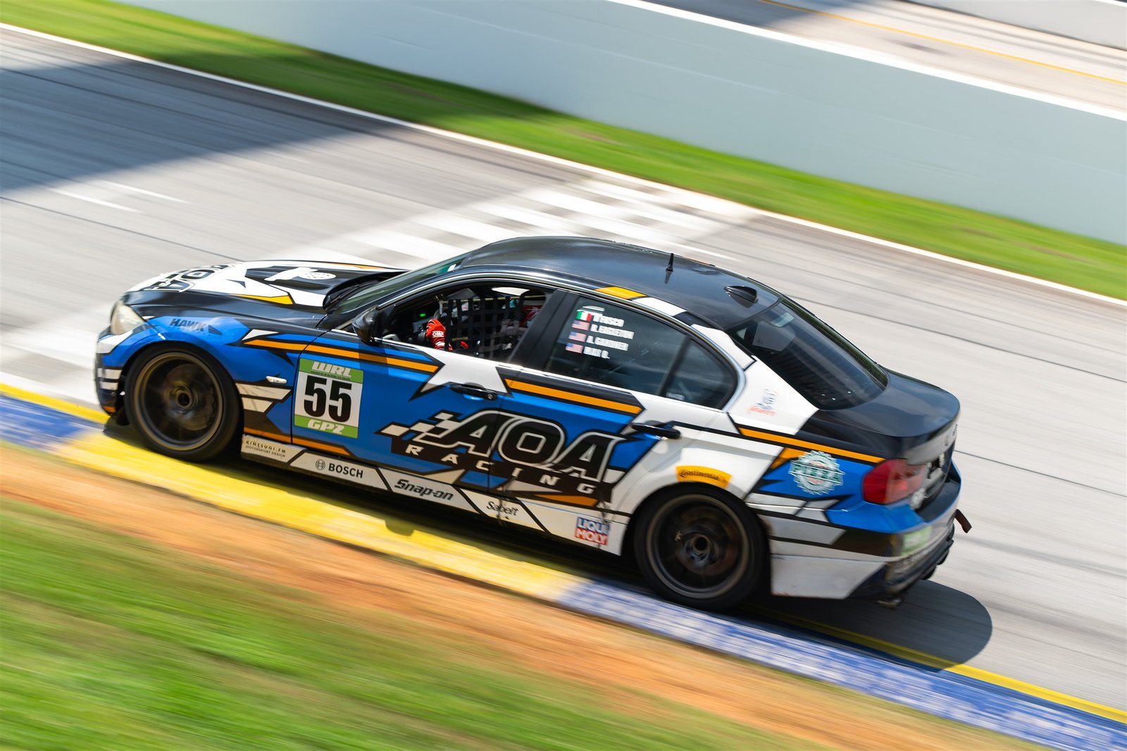 El BMW número 55 de AOA Racing, de la categoría GP2 del World Racing League, pasa a gran velocidad por una curva con pianos amarillos.