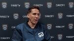 Mikey Varas, entrenador de San Diego FC, habla en conferencia de prensa frente a un fondo con el escudo del club.