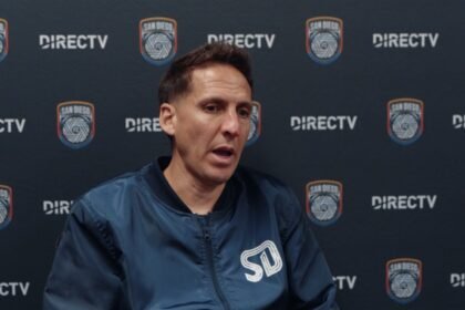 Mikey Varas, entrenador de San Diego FC, habla en conferencia de prensa frente a un fondo con el escudo del club.