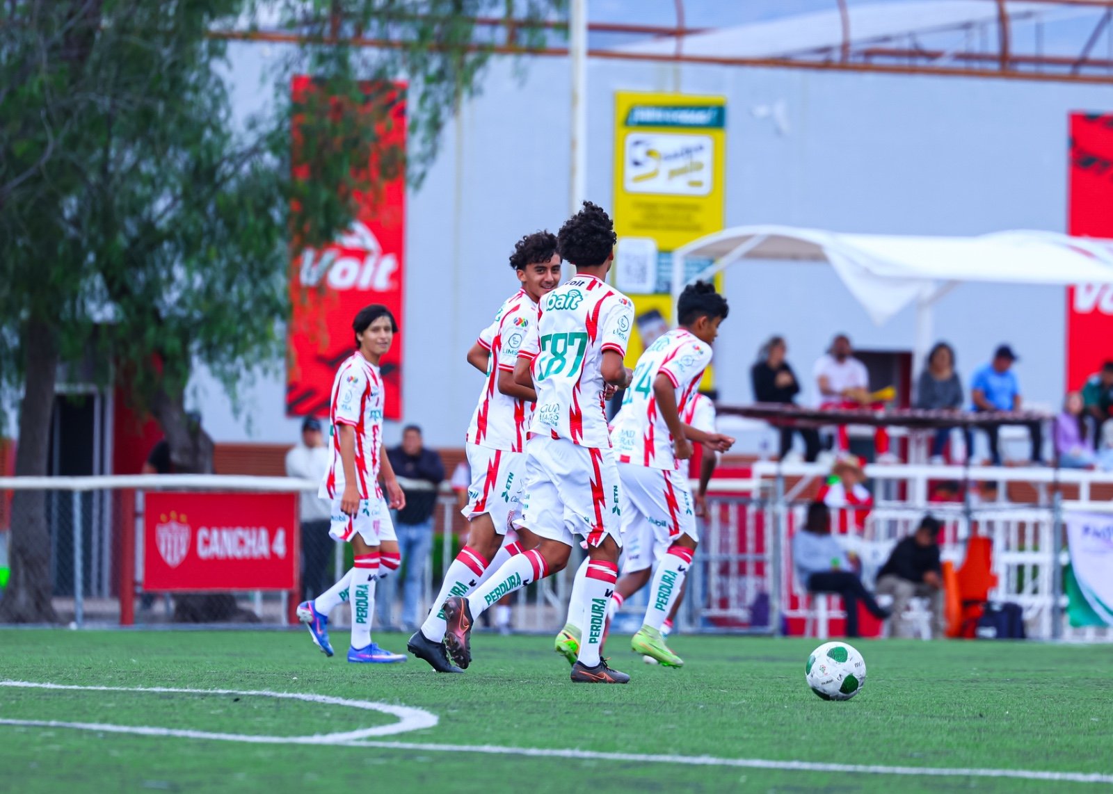 Jugadores de los Rayos de Necaxa con playera blanca y roja corren en la cancha 4 de Casa Club Necaxa