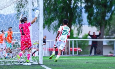 Un jugador de Necaxa con el número 324 corre junto a la portería mientras el portero rival levanta los brazos en un partido de la TDP