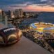 Ilustración conceptual sobre si los dueños de los Padres pueden comprar a los Chargers: un balón con rayos de los Chargers y costuras de béisbol frente a un estadio imaginario en San Diego.