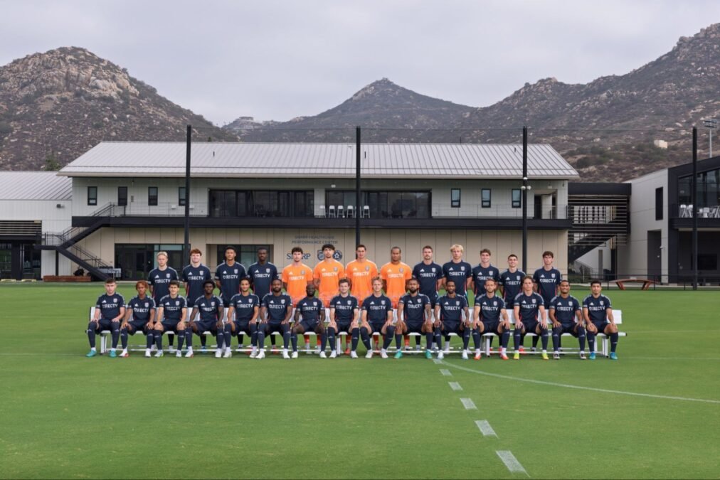 Foto oficial de la plantilla de San Diego FC, con jugadores de playera azul marino, porteros de naranja y las montañas al fondo, en el centro de entrenamiento.