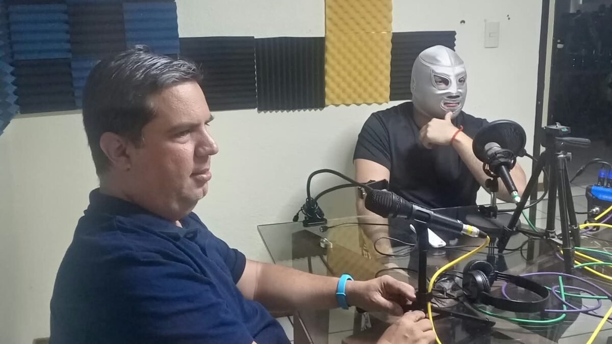El Santo Jr., con su máscara plateada, durante la entrevista en una cabina de radio junto a un conductor.