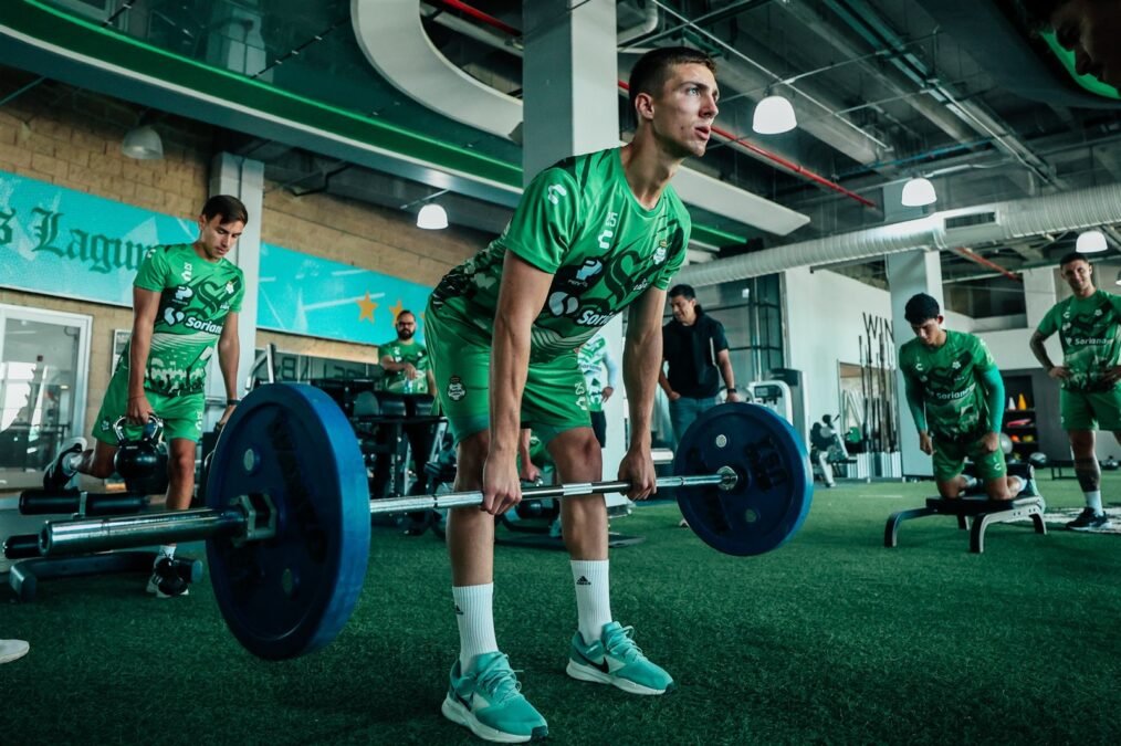 Santos: ¿Liguilla? ¡Felipe Sánchez pide pies en la tierra! 2 Un jugador de Santos Laguna levanta una barra con pesas en el gimnasio del club durante la preparación, con compañeros al fondo.