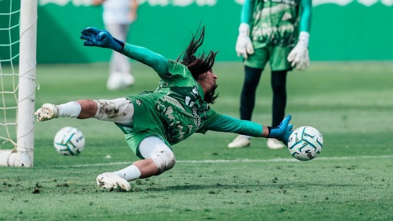 Un portero de Santos Laguna se estira para atajar el balón durante un entrenamiento, con otro portero de pie al fondo.