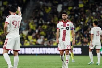 Mediocampista de Toronto FC con el número 21 y el brazalete de capitán, en un partido de la MLS, con dos compañeros al fondo.