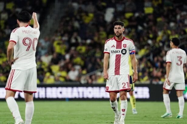 Mediocampista de Toronto FC con el número 21 y el brazalete de capitán, en un partido de la MLS, con dos compañeros al fondo.